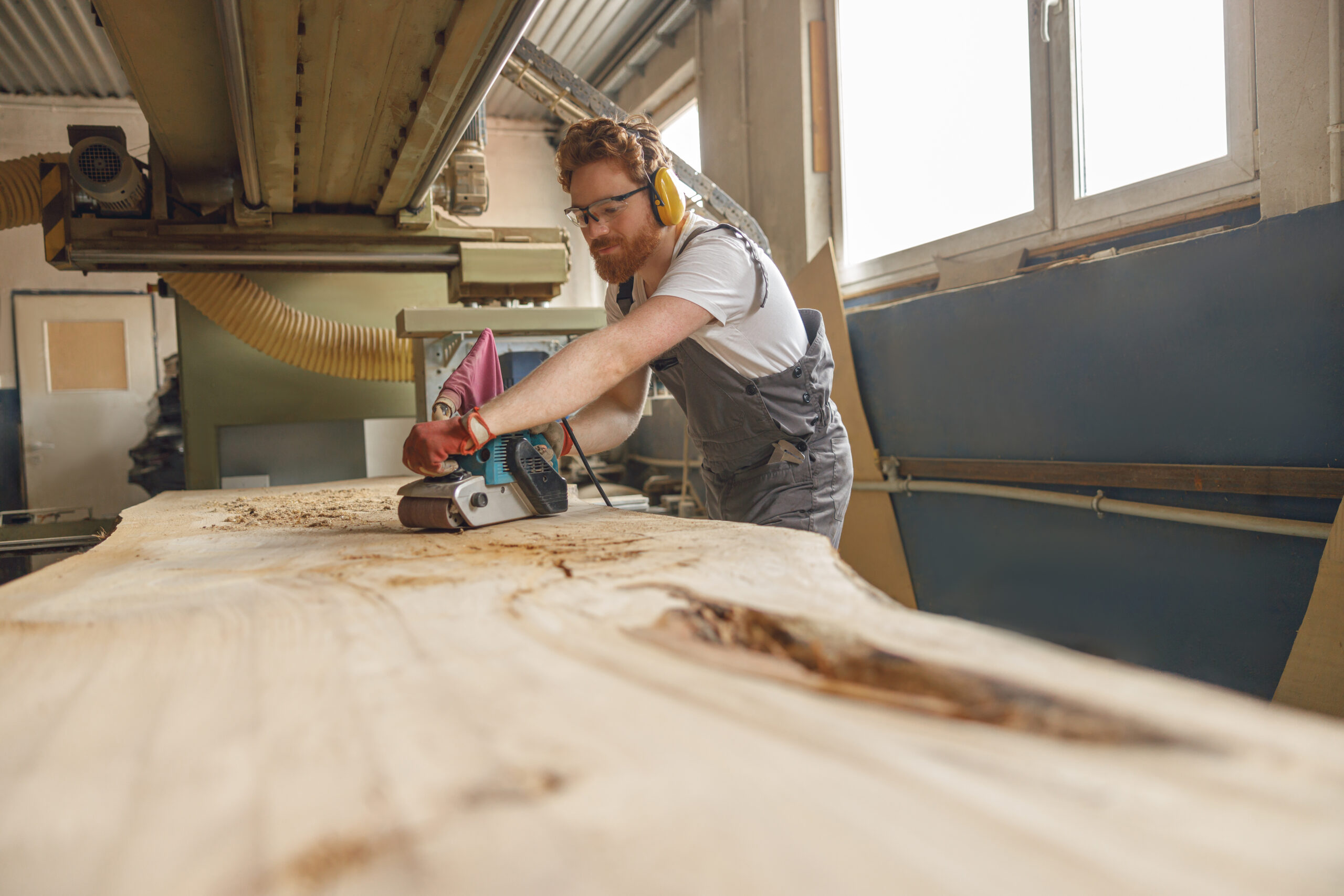 Professional male carpenter using electric sander for wood. Manufacture of wood products