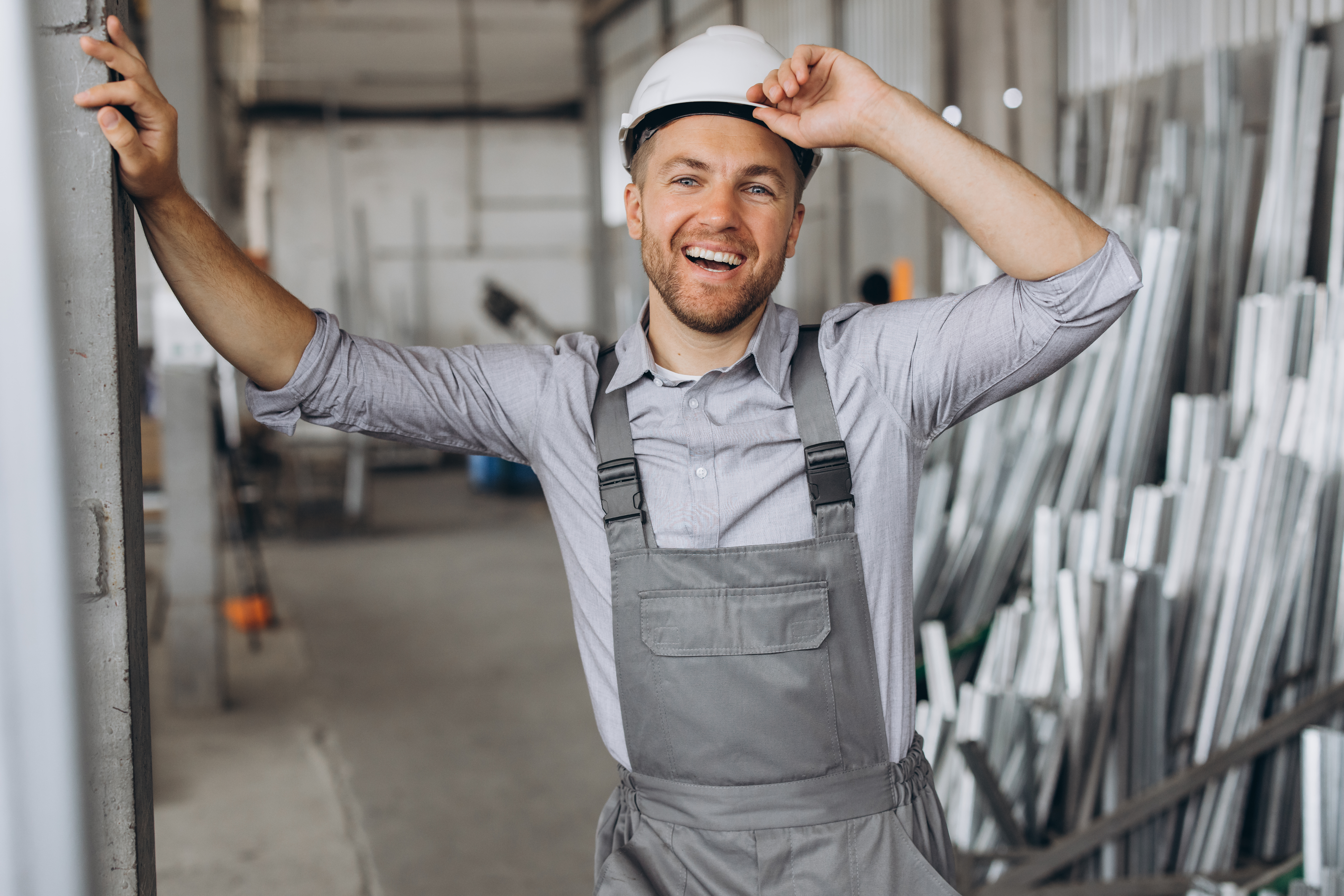 Portrait of a happy worker in a gray uniform and a white hard hat posing on the background of factory production